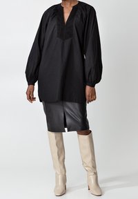 Svart, långärmad tunika med en texturerad, V-formad halsringning, ihop med en figurnära svart läderskirt och knähöga beige klackstövlar.