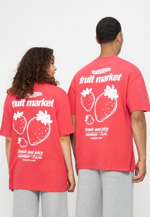 Két ember piros pólót visel fehér eper-illusztrációkkal és a "fruit market fresh and juicy Sundays 2 p.m." felirattal a hátukon.