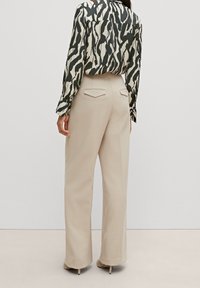 Beige wide-leg trousers with a smooth texture, featuring two back pockets and a clean cut. Paired with a black-and-white patterned blouse.