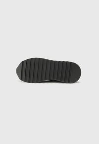 Semelle de chaussure en caoutchouc noir, dotée de rainures horizontales pour l'adhérence, d'un orteil arrondi et d'une section de talon lisse. Design minimalist sans logos visibles.