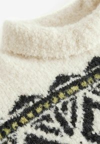 Pull en tricot avec un col montant, présentant une texture crémeuse duveteuse et un motif de feuilles noires et vertes le long de l'ourlet.