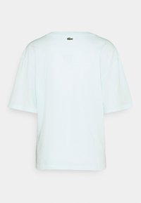 T-shirt bleu clair à manches courtes en coton. Il possède un col rond et un petit logo Lacoste brodé près du col.