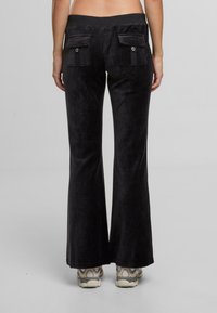 Czarne spodnie typu dzwony z miękkiego, teksturowanego materiału. Posiadają dwie tylne kieszenie z klapką i szeroki pas. Noszone z beżowymi trampkami.