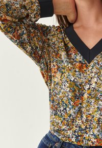 Floral blouse in vibrant colors including yellow, blue, and white. Features a V-neckline and long sleeves with elastic cuffs.