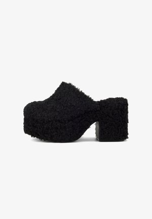 Zwarte pluizige klompen met een gestructureerd bovenwerk, een dikke plateauzool en blokhak. Het oppervlak is zacht, lijkt op pluche stof, met een afgeronde neus.