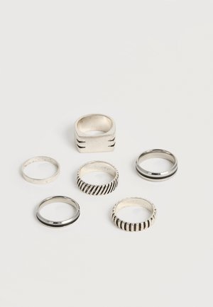 Hat ezüst gyűrű változatos mintákkal, beleértve sima sávokat, bordázott textúrákat és egy vastag, négyzet alakú gyűrűt, amelyek egy sima fehér felületen vannak elrendezve.