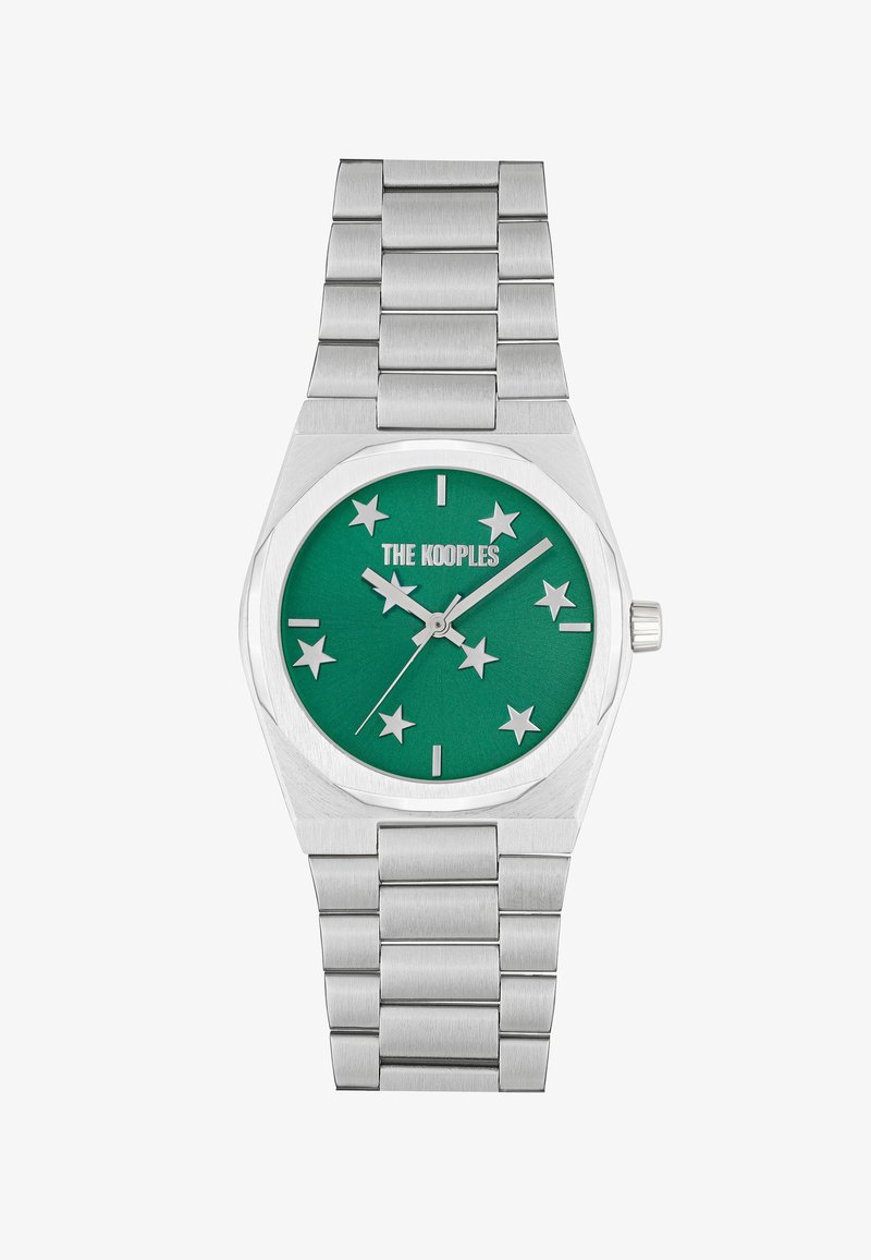 Suds ar sudraba metāla pulksteni ar pulētu apdari, kas izceļas ar zaļo ciparnīcu, zvaigžņu atzīmēm un teksturētu nerūsējošā tērauda siksniņu.