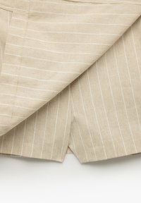 Beige Leinen-Shorts mit weißen vertikalen Streifen, die eine saubere Verarbeitung und subtile Textur aufweisen. Der Stoff wirkt leicht und atmungsaktiv.