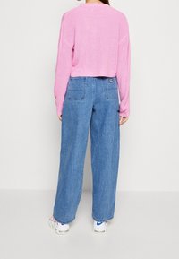 Rosa, gerippter, cropped Pullover mit langen Ärmeln, kombiniert mit weit geschnittenen, hellblauen Jeans aus Denim, die eine Gesäßtasche und ein Logoshäggchen haben.