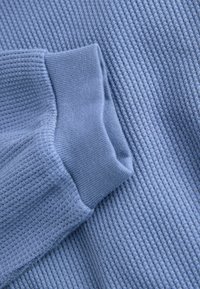Tessuto azzurro chiaro con una trama a nido d'ape, caratterizzato da un elegante dettaglio ai polsini. Colore uniforme con un aspetto morbido.