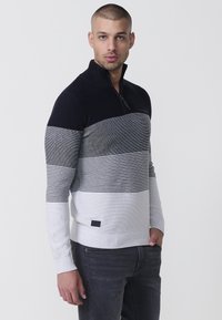 Strickpullover mit halbem Reißverschluss, ausgestattet mit horizontalen Streifen in Schwarz, Grau und Weiß. Glatte Textur und gerippte Bündchen, mit einem Logodetail.