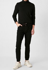 Maglione nero a collo alto realizzato in tessuto morbido, abbinato a pantaloni jogger neri con vita elastica e dettagli con cordini.