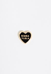 Spilla a forma di cuore dorato con un centro in smalto nero, caratterizzata dal testo in rilievo "BIMBA Y LOLO" in lettere grasse.