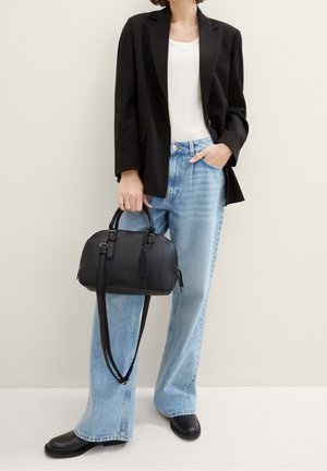 Kvinde iført sort blazer, hvid top, lyseblå jeans med vide ben, sorte sko, og bærer en sort læderhåndtaske med skulderrem.