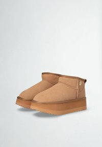 Beige suede ankle boots with a rounded toe, short shaft, and a thick, textured tan rubber platform sole. Features a small logo accent.
