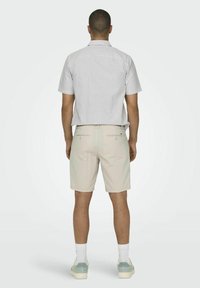 Lyhythihainen, vaaleanharmaa raidoitettu paita, beigeet lyhyet housut, joissa on tekstuuripainatus, yhdistettynä valkoisiin sukkiin ja vaaleansinisiin tennareihin.