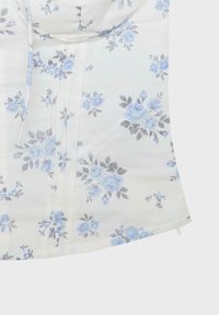 Tissu blanc avec un motif de roses bleu clair et de feuilles grises, présentant des coutures et un bord partiel visible sur un fond uni.