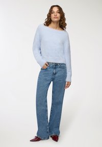 Maglione fuzzy azzurro chiaro con scollatura ampia, abbinato a jeans in denim chiaro a vita alta. Le scarpe sono ballerine a punta rosso scuro.