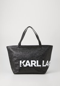 Juodas blizgus pirkinių maišas su dviem rankenėlėmis, su įspaustu tekstūru ir dideliais baltais užrašais "KARL LAGERFELD" vienoje pusėje.
