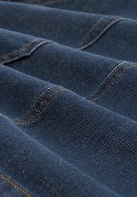 Mørkeblå denimstoff med synlig tekstur, foldet med kontrasterende orange stikninger og subtile prikker gennem hele stoffet.