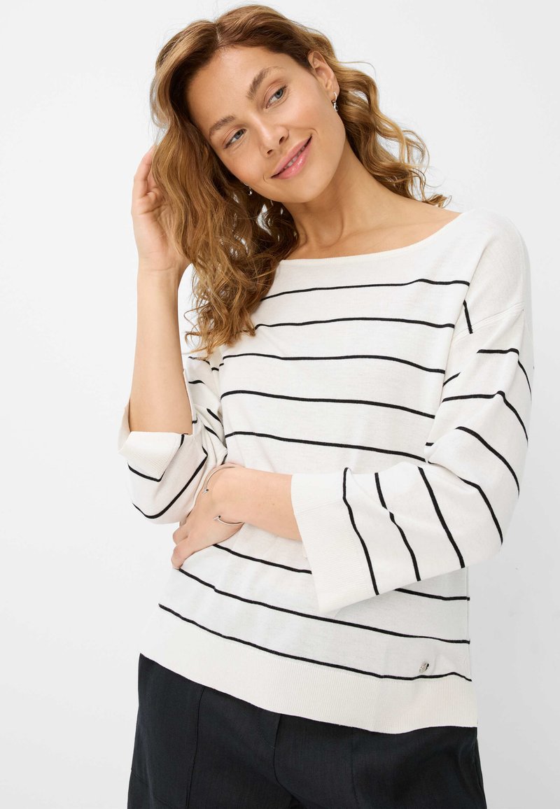Pull blanc avec des rayures horizontales noires, décolleté bateau, manches trois-quarts et détail sur les côtés. Le tissu semble doux et tricoté.