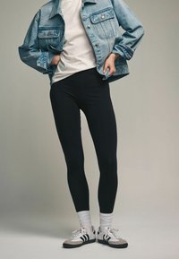 Crne tajice u kombinaciji s bijelom majicom, preko kojih je lagana svijetloplava traper jakna. Sivu i bijelu tenisicu dopunjuju ovaj outfit.