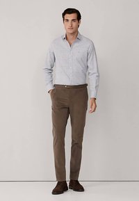 Niebiesko-biała koszula w kratę, dopasowana, połączona z brązowymi, dopasowanymi spodniami i ciemnobrązowymi butami. Gładka tkanina o strukturze konstrukcyjnej.