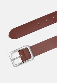 Ceinture en cuir marron avec une boucle rectangulaire en métal argenté, arborant le nom de la marque "TOM TAILOR". Comprend des trous pour l'ajustement des tailles.