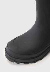Botte en caoutchouc noir avec une surface texturée, un embout renforcé et une semelle à crans profonde conçue pour l'adhérence et la durabilité.