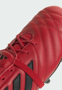 Scarpette da calcio in pelle rossa con texture trapuntata, dettagli neri e cinturino elastico. Presentano un design lineare e una silhouette a profilo basso.