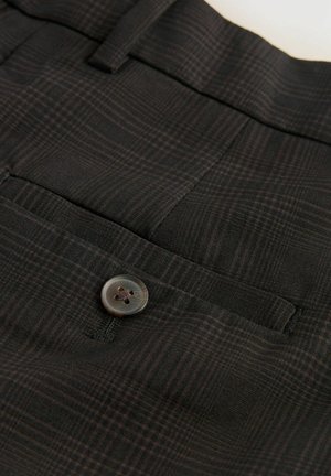 Černá vzorovaná tkanina s jemným mřížkovým designem. Obsahuje kulatý plastový knoflík se čtyřmi otvory, přišitý do oblasti pasu.