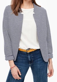 Blazer rayé en marine et blanc, associé à un haut blanc et un jean bleu. Accentué par une ceinture jaune. Tissu lisse, design décontracté.