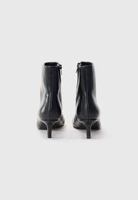 Stivaletti neri in pelle, con chiusura a zip, tacco affusolato e texture liscia, caratterizzati da una silhouette aderente e un design minimalistico.