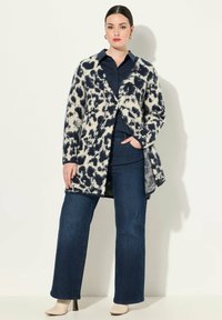 Stickad cardigan med ett leopardmönster i marinblått och krämvitt. Har en öppen front, långa ärmar och en avslappnad passform. Kombinerad med mörka jeans.