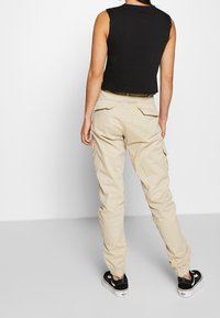 Černý zkrácený top bez rukávů v kombinaci s béžovými cargo kalhotami s kapsami a elastickými manžetami. Černé tenisky dokreslují celý outfit.