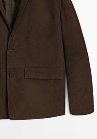 Blazer in suede marrone con una tasca sul petto, due bottoni e una forma strutturata. Texture liscia e finitura su misura.