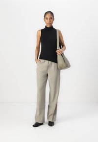 Top noir sans manches à col roulé, pantalon large beige clair, et sac à bandoulière gris. Tissu lisse et chaussures noires brillantes.