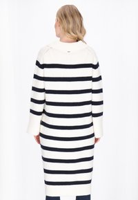 Tunic in maglia color crema con strisce orizzontali blu navy, caratterizzata da un colletto a rolo, maniche lunghe e texture a costine. Design di lunghezza media.