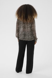 Blusa leggera e trasparente con maniche lunghe, caratterizzata da un motivo leopardato in tonalità di marrone. Abbinata a pantaloni neri, morbidi e di taglio comodo.
