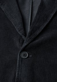 Černý kordový blejzr s výstřihovým límcem, zapínáním na knoflíky vpředu a svislou ribkovou texturou. Vysoce detailní vzor látky viditelný.