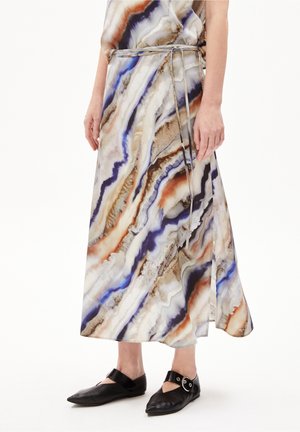 Kvinde iført en midilang nederdel med multifarvet, abstrakt mønster, en tynd bælte og sorte flade sko med spids tå og ankelremme.