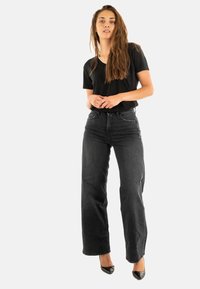 Camiseta negra de mangas cortas combinada con unos vaqueros negros de tiro alto y pierna recta; modelo llevando unos zapatos de tacón alto negros brillantes.