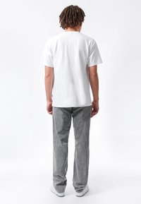 Camiseta blanca de algodón de manga corta, combinada con pantalones grises texturizados. El conjunto incluye zapatillas blancas y una branding minimalista en la tela.