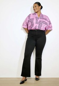 Blusa de manga corta con estampado rosa y cuello camisero, combinada con pantalones negros de tiro alto y campana, y bailarinas negras de puntera puntiaguda.