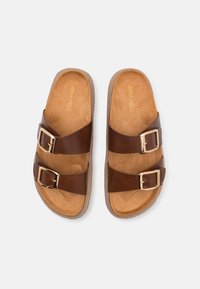 Brune dobbelspændte sandaler med en glat læderoverdel, tan-dæmpet sål og en tekstureret gummisål. Guldtonede spænder giver detaljer.