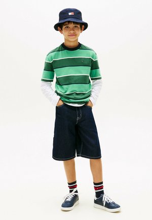 Dreng iført en navy bøllehat, grønstribet t-shirt over en hvid langærmet trøje, navy shorts, stribede strømper og navy sneakers.