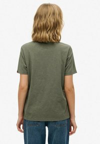 Camiseta verde oliva de algodón suave, de manga corta, cuello redondo, corte recto, con una pequeña etiqueta de la marca en la manga izquierda.