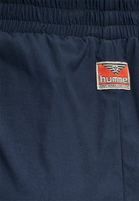 Blaue Stoffshorts mit einem elastischen Bund und einem "hummel" Logo-Tag in Rot und Weiß im Taschenbereich. Angenehme Textur, lässiges Design.