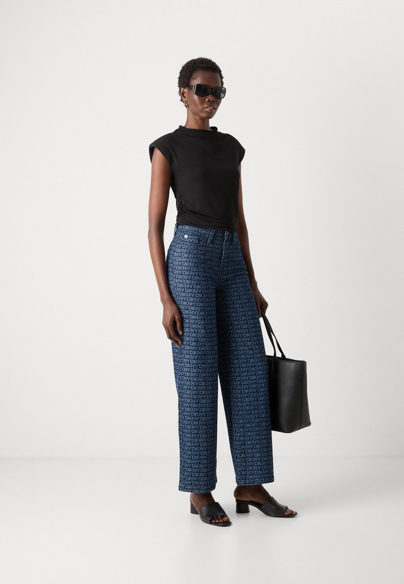 Top negro ajustado con mangas cortas, pantalones anchos de rayas azules, sandalias negras de tacón cuadrado y un bolso negro.