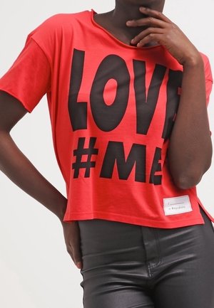 Rood cropped t-shirt van lichtgewicht stof, met grote zwarte tekst "LOVE #ME." Heeft een losse pasvorm en een iets oversized halslijn.